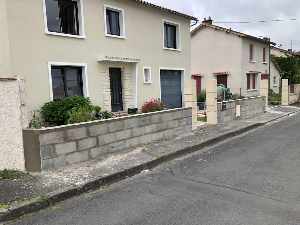 Muret de clôture en parpaings avec piliers enduits devant une maison, en bord de rue à Niort