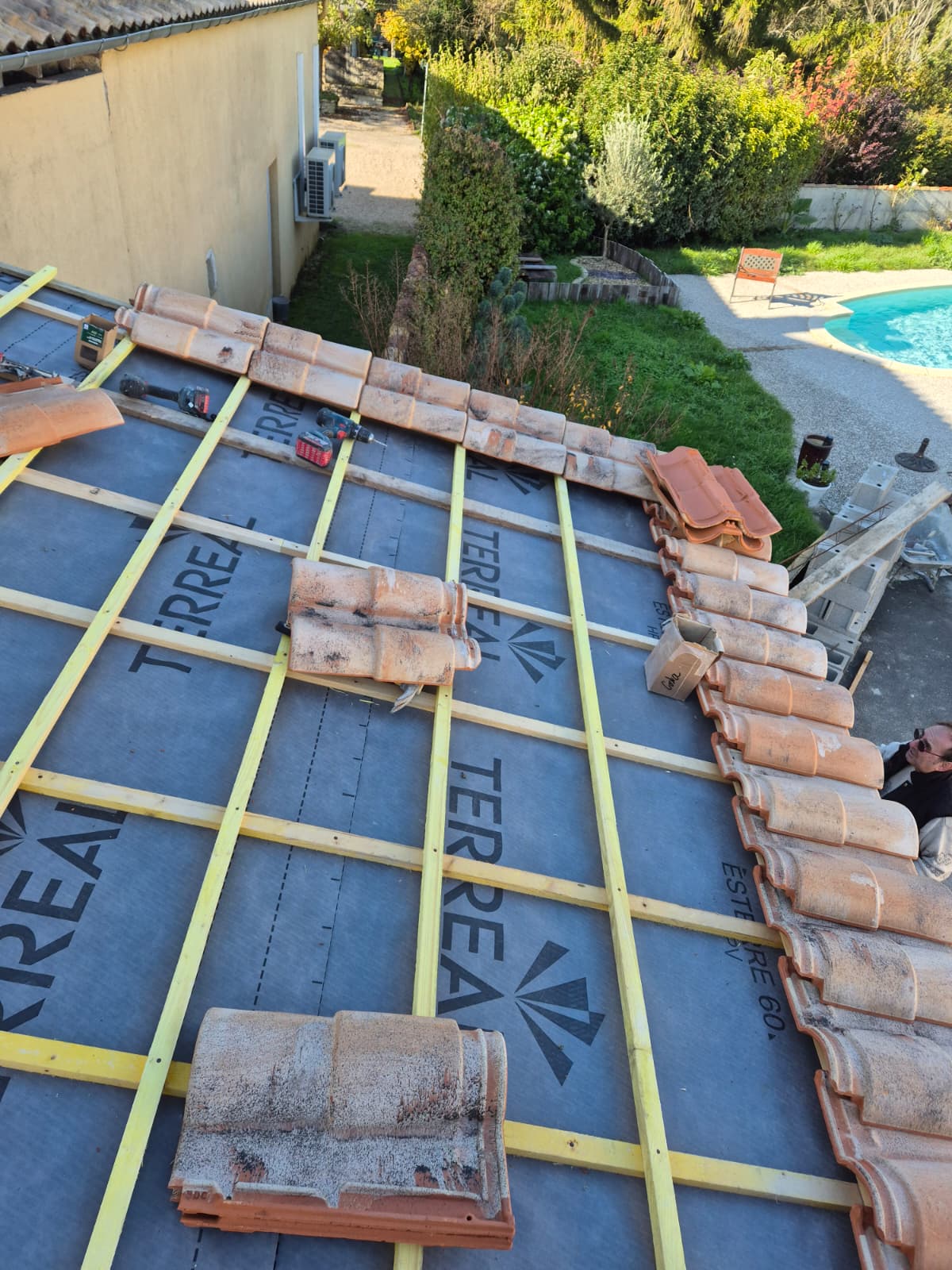 Réfection de toiture en cours avec pose de tuiles TERREAL sur liteaux, jardin en contrebas